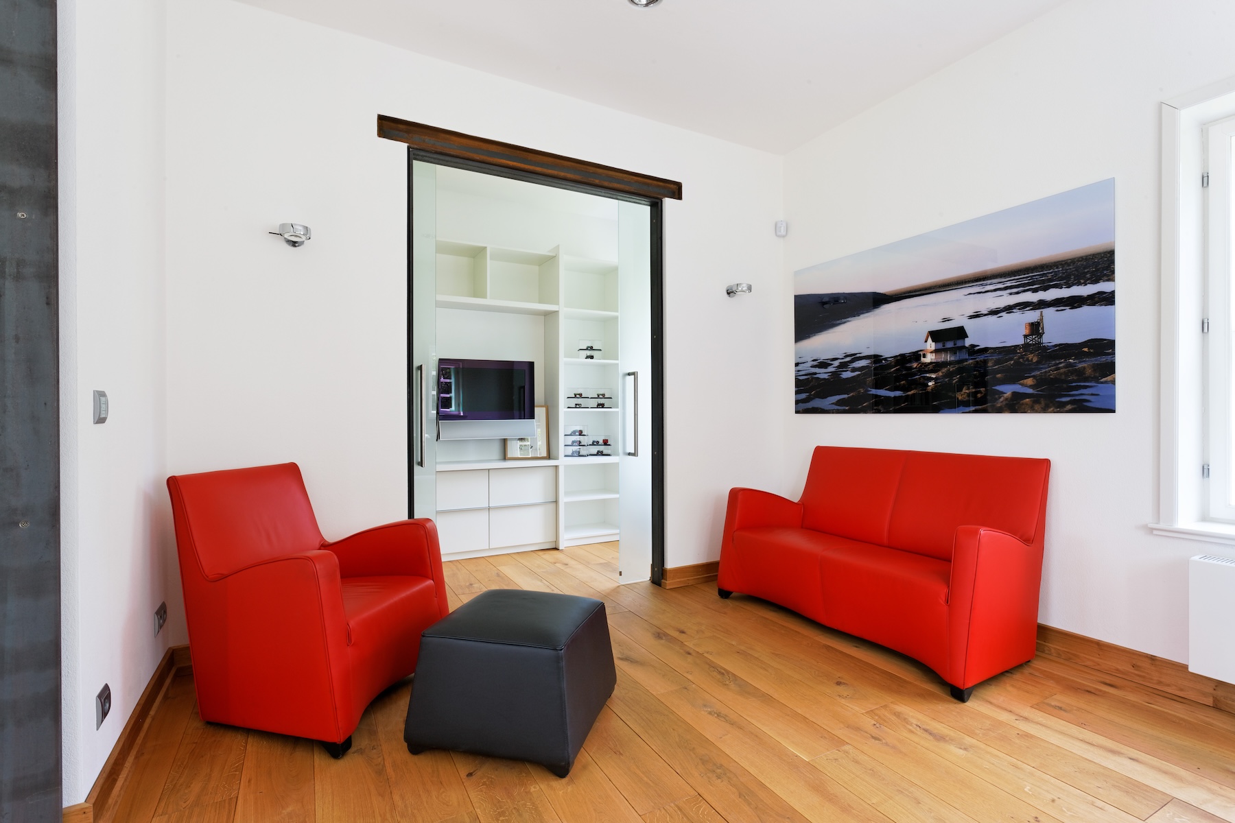 Zwei rote Sofas und ein schwarzer Hocker in einem modernen Raum mit Holzfußboden.